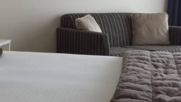 A hotel room with a bed, a grey sofa, and a white nightstand.