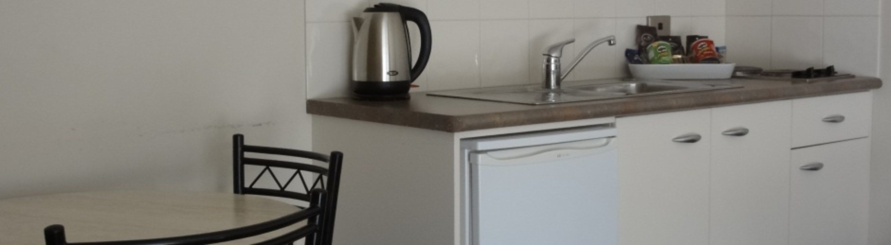 A small kitchenette with a coffee maker, sink, and cabinets.