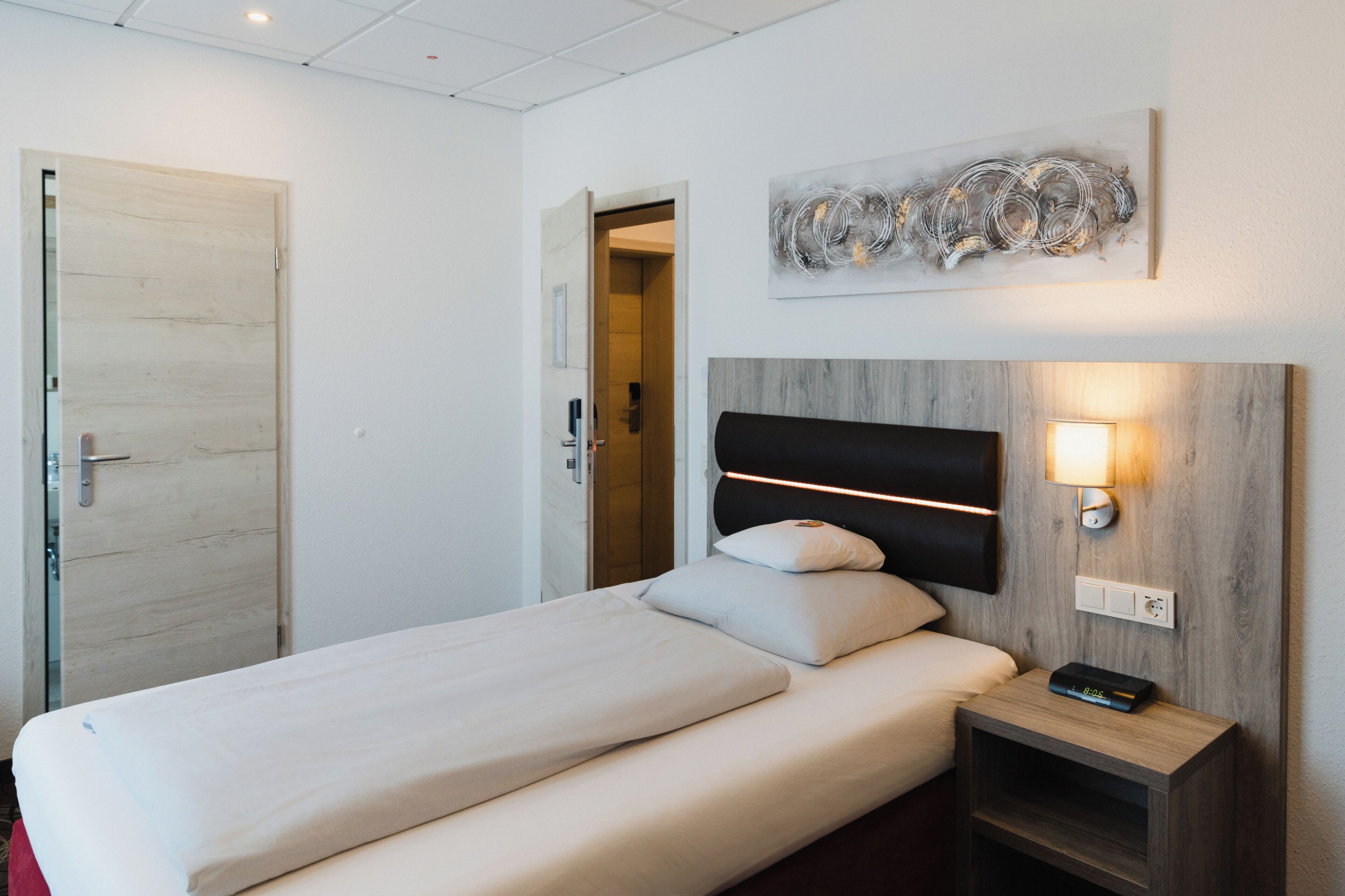 Una habitación de hotel con una cama, una mesita de noche y un aplique de pared.