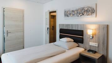 Una habitación de hotel con una cama, una mesita de noche y un aplique de pared.