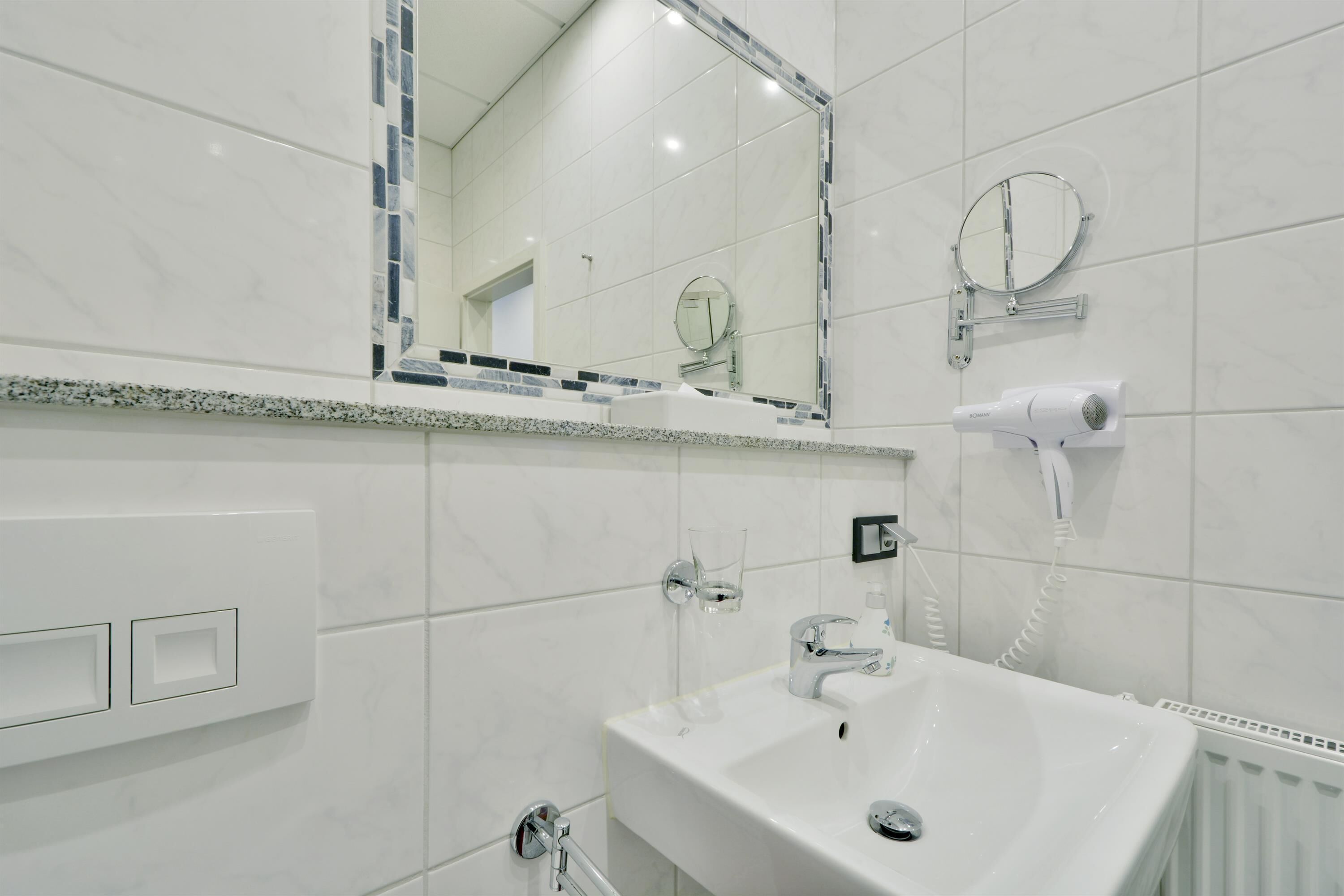 Ein modernes Badezimmer mit Waschbecken, Spiegel, Fön und Handtuchhalter.