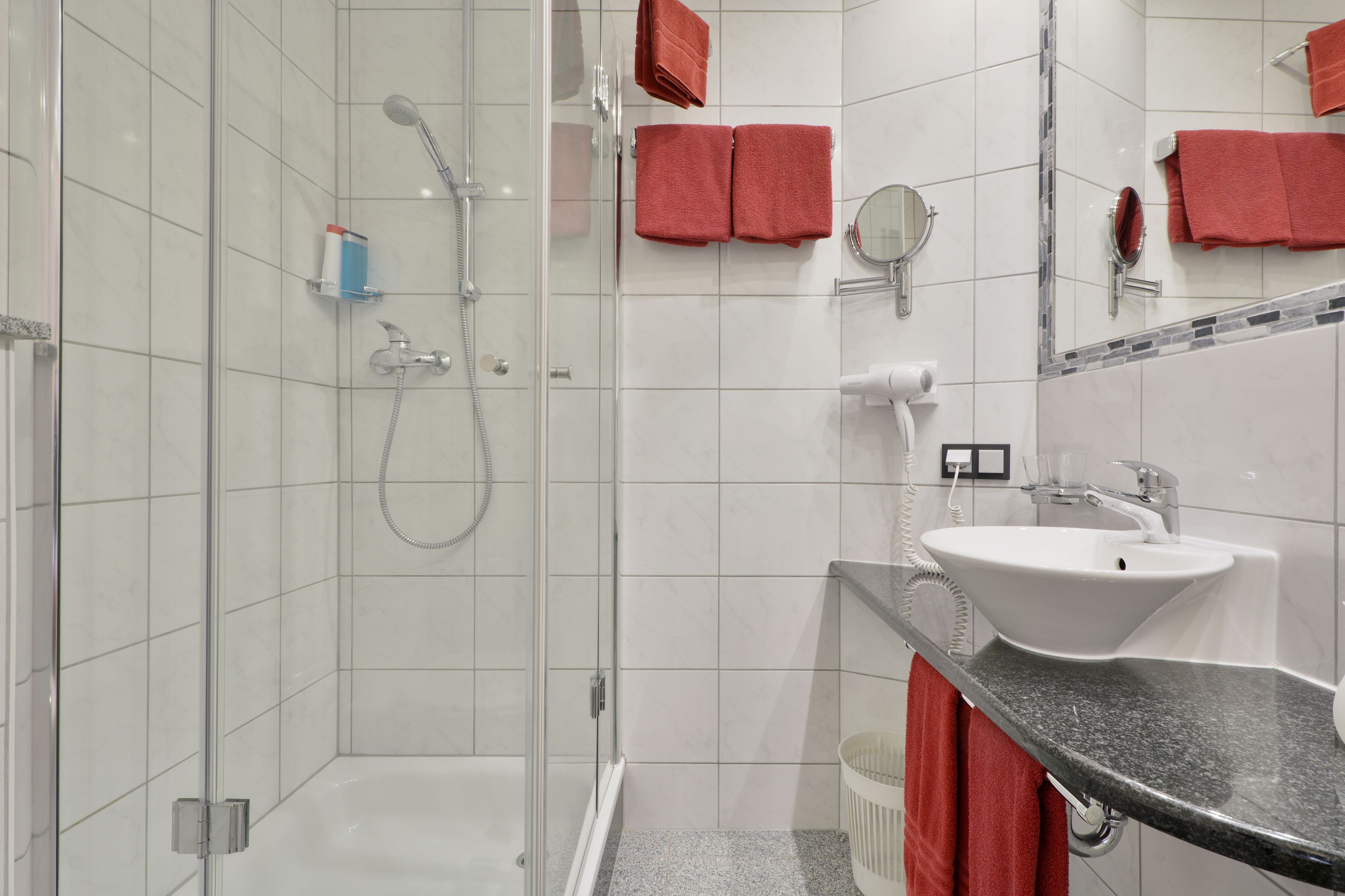 A modern bathroom with a glass-enclosed shower, a white sink, and red towels.