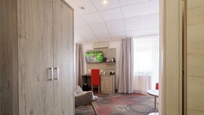 A hotel room with a wooden wardrobe, a desk with a red chair, a television, and a round table. - Hotel Engelhorn (Leimen)