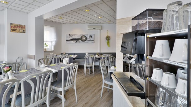 A modern cafe with white furniture, a coffee machine, and a menu board. - Hotel Engelhorn (Leimen)