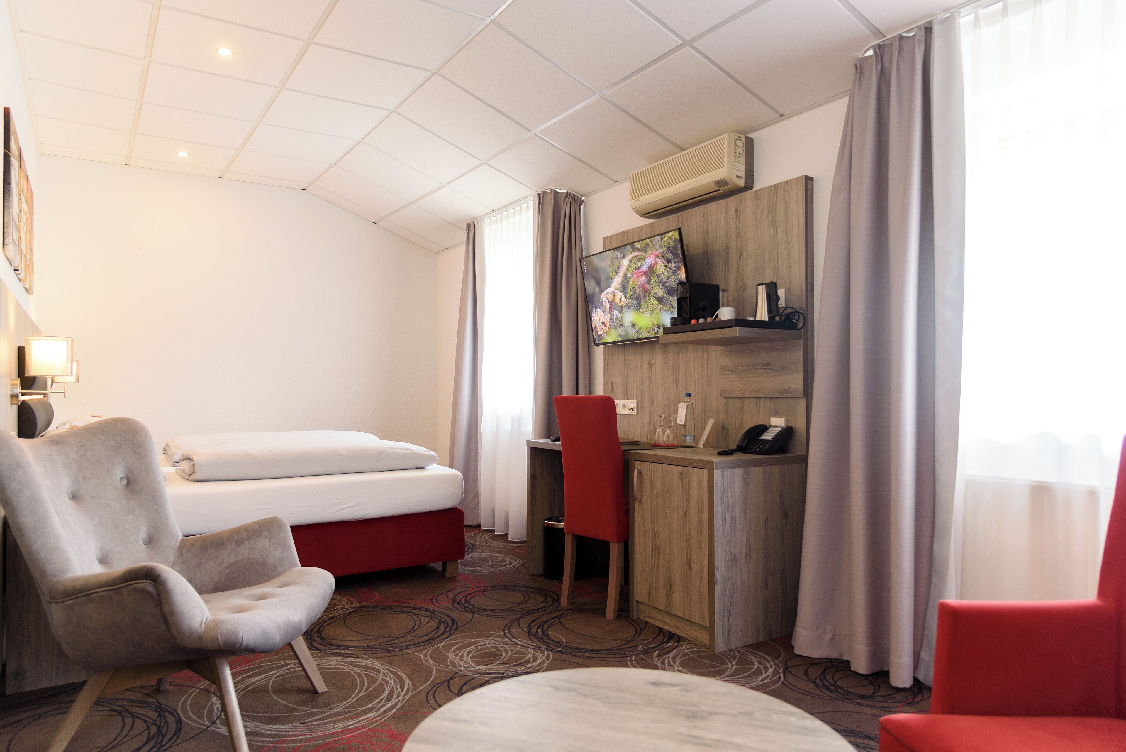 Quarto de hotel com cama, escrivaninha, cadeira, televisão e minibar.