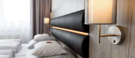 A modern hotel room with a large bed, a headboard with integrated lighting, and a wall-mounted lamp.