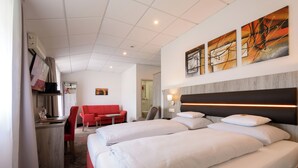 A hotel room with two beds, a desk, a red sofa, and artwork on the wall. - Hotel Engelhorn (Leimen)