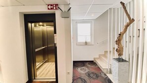 A hallway with an elevator, a staircase, and a decorative sculpture. - Hotel Engelhorn (Leimen)