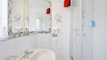 Un baño moderno con un lavamanos blanco, dos espejos, una cabina de ducha de vidrio y una toalla roja.