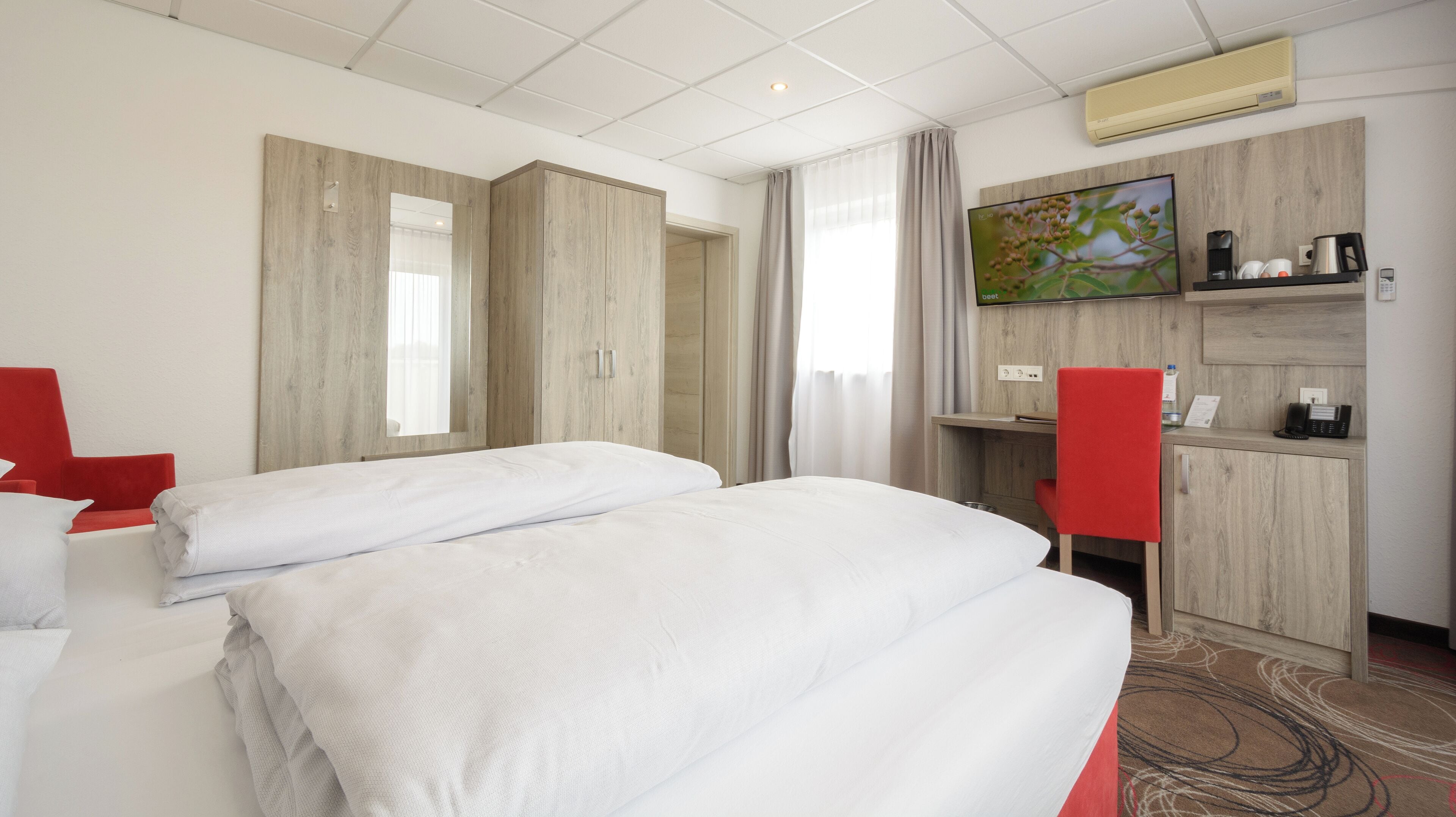 A hotel room with two beds, a desk, a chair, and a TV.