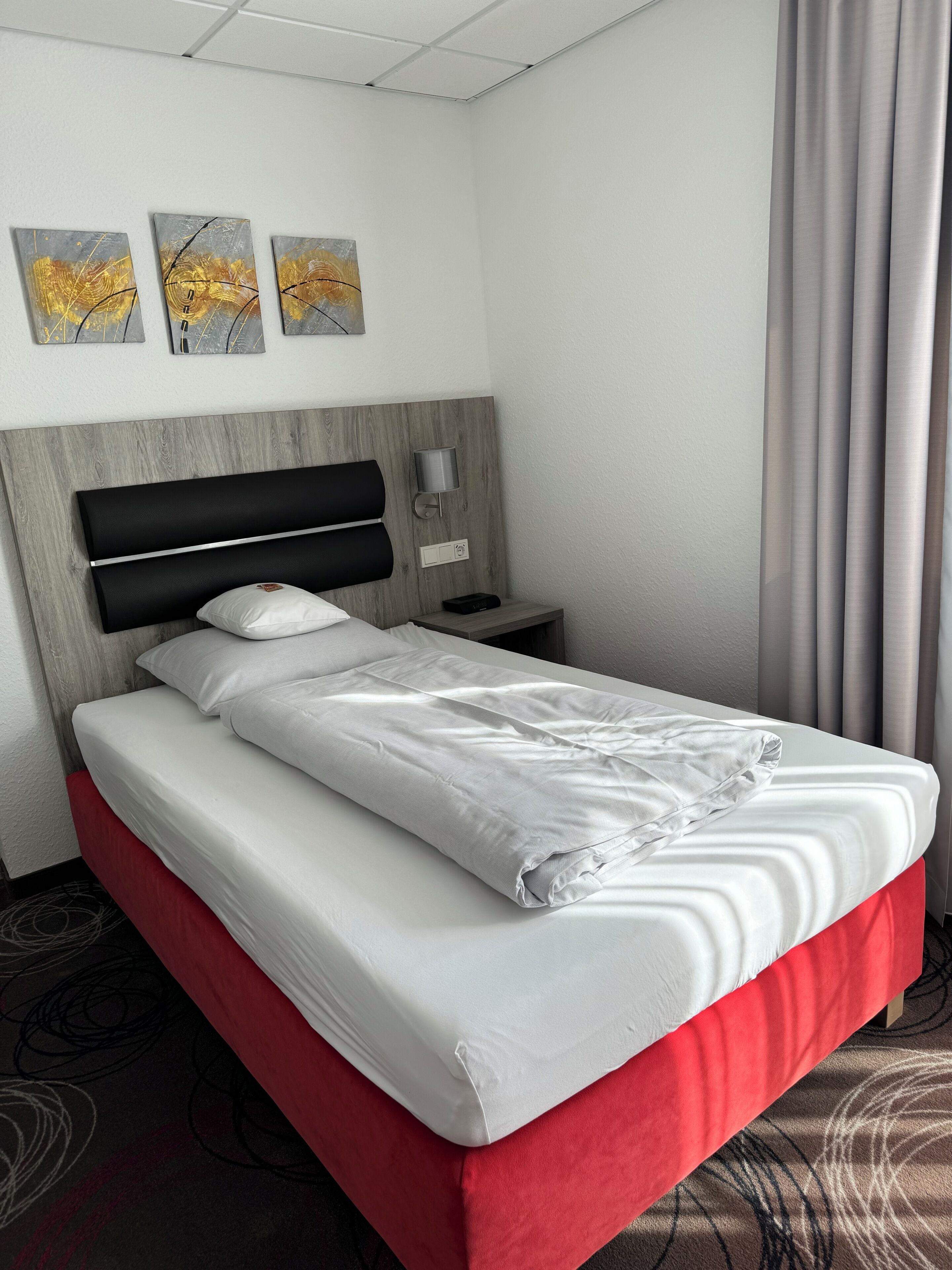 A hotel room with a bed, a nightstand, a lamp, and artwork on the wall.