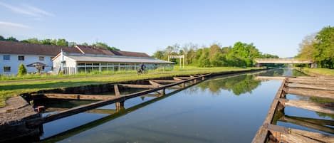 Un canal bordé d’une promenade en bois, une maison et un pont en arrière-plan.
