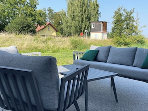 An outdoor seating area with a sofa and chairs, a small table, and a view of a house and trees.