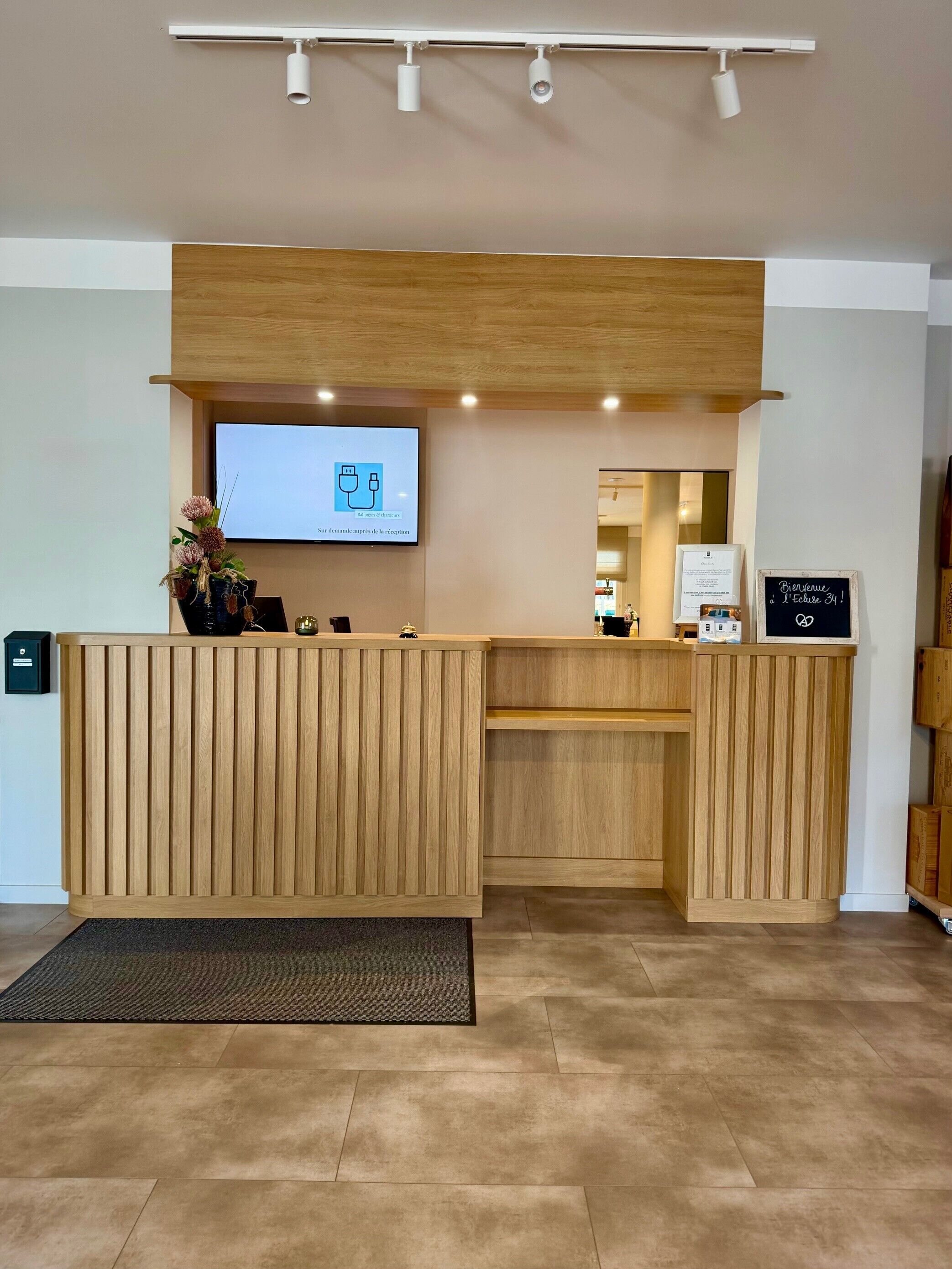 Una mesa de recepción con un televisor de pantalla plana, paneles de madera y un cartel de bienvenida.