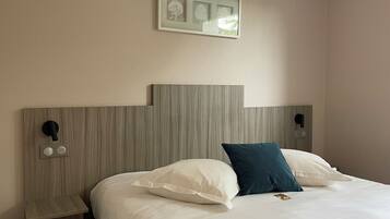 Ein Hotelzimmer mit Bett, Nachttisch, einem an der Wand befestigten Bilderrahmen und einer Steckdose.