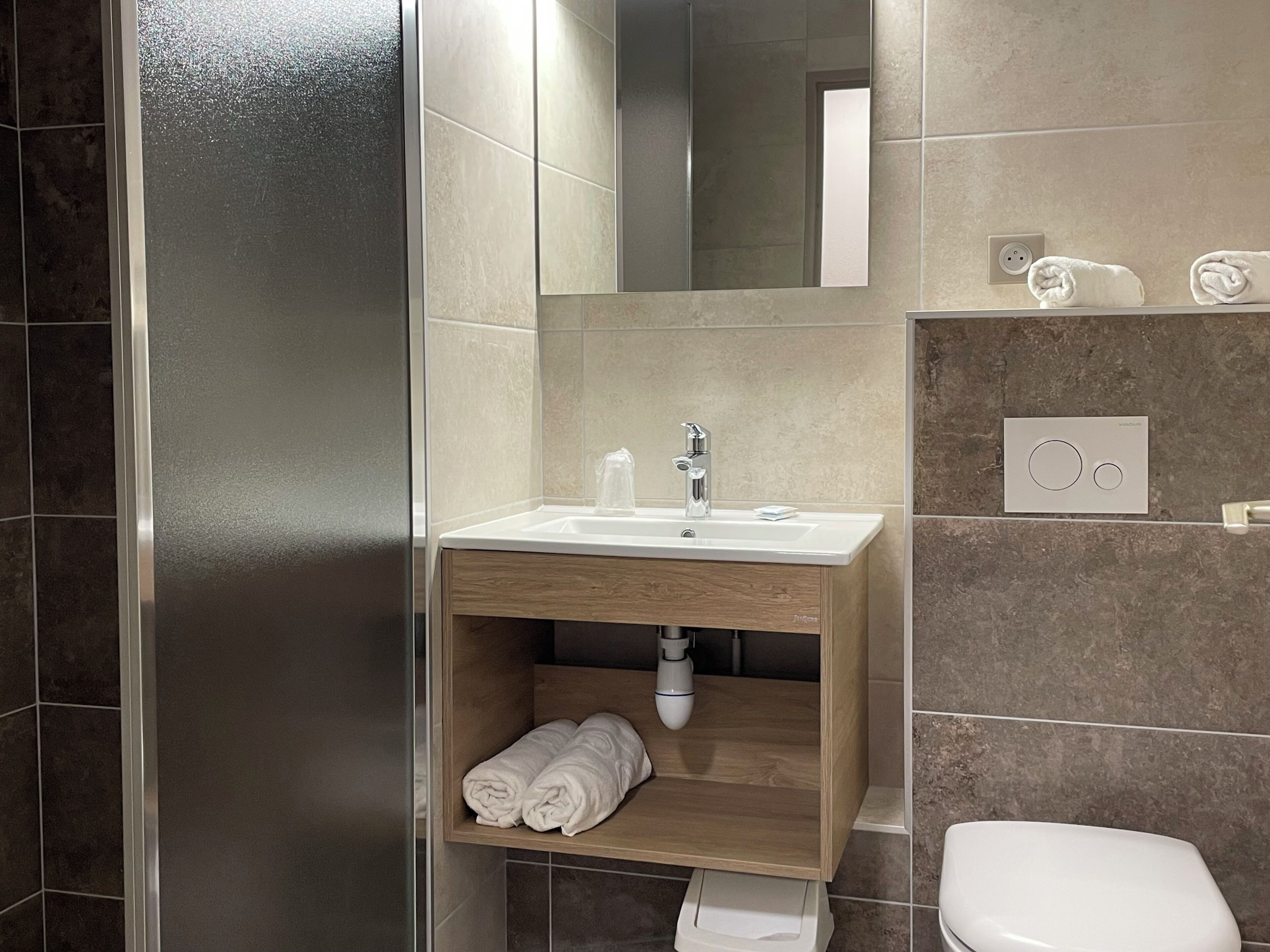 Un baño moderno con cabina de ducha de vidrio, tocador de madera con lavamanos y un inodoro.