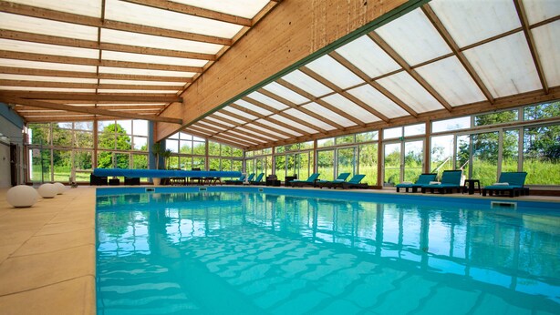 Una piscina techada con sillas reclinables azules y vistas al exterior.