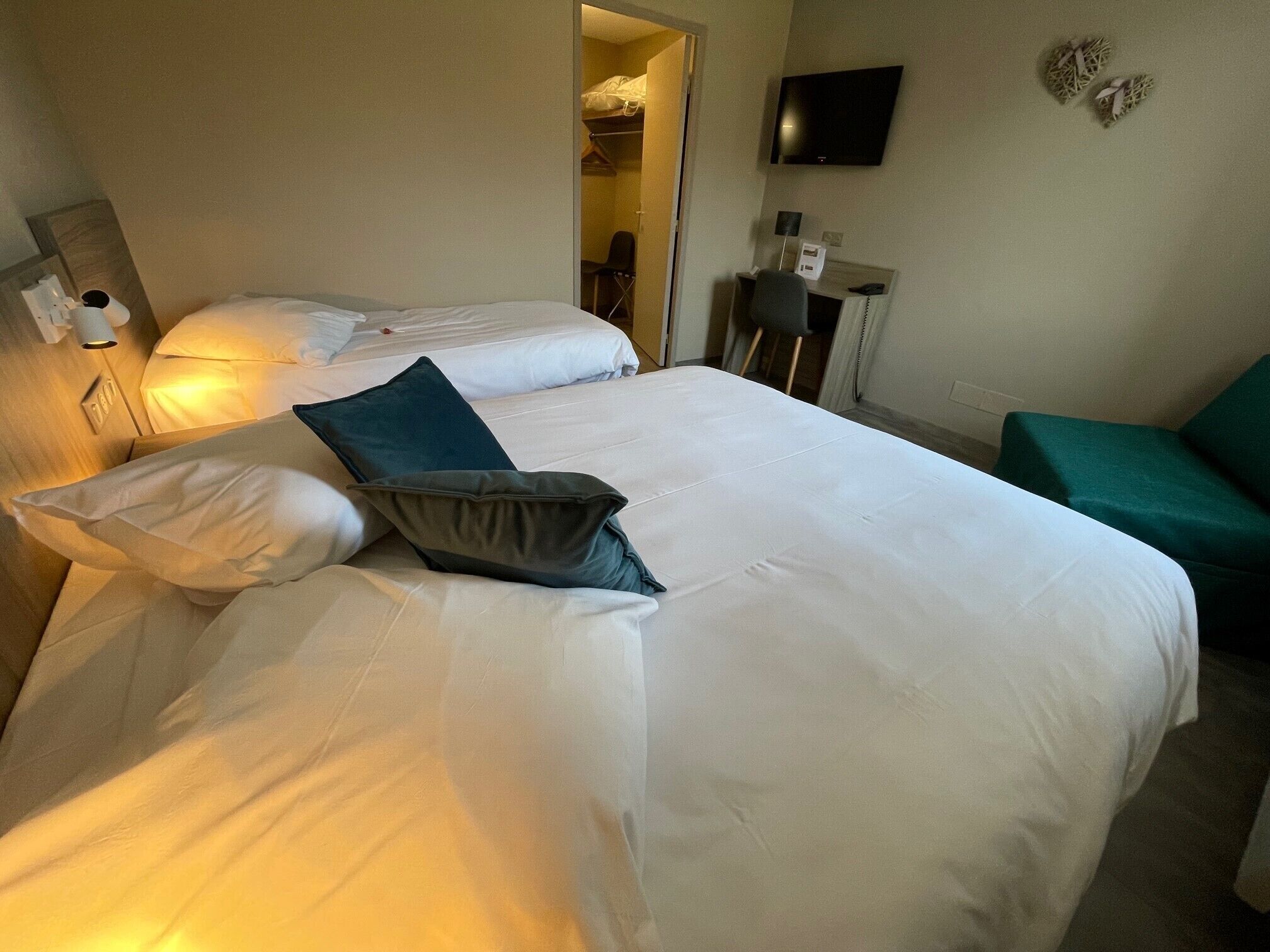 Een hotelkamer met een groot bed, een bureau met stoel, een televisie en een groene fauteuil.