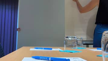 A meeting room with a whiteboard, blue pens, papers, and a glass of water on the table.