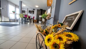 Un área de recepción con un carrito de madera lleno de girasoles y trigo, una pizarra con un mensaje de bienvenida y un espacio de asientos con sillas y mesas.