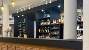 Zona de bar con estantes de botellas de licores, vasos y una máquina de café.