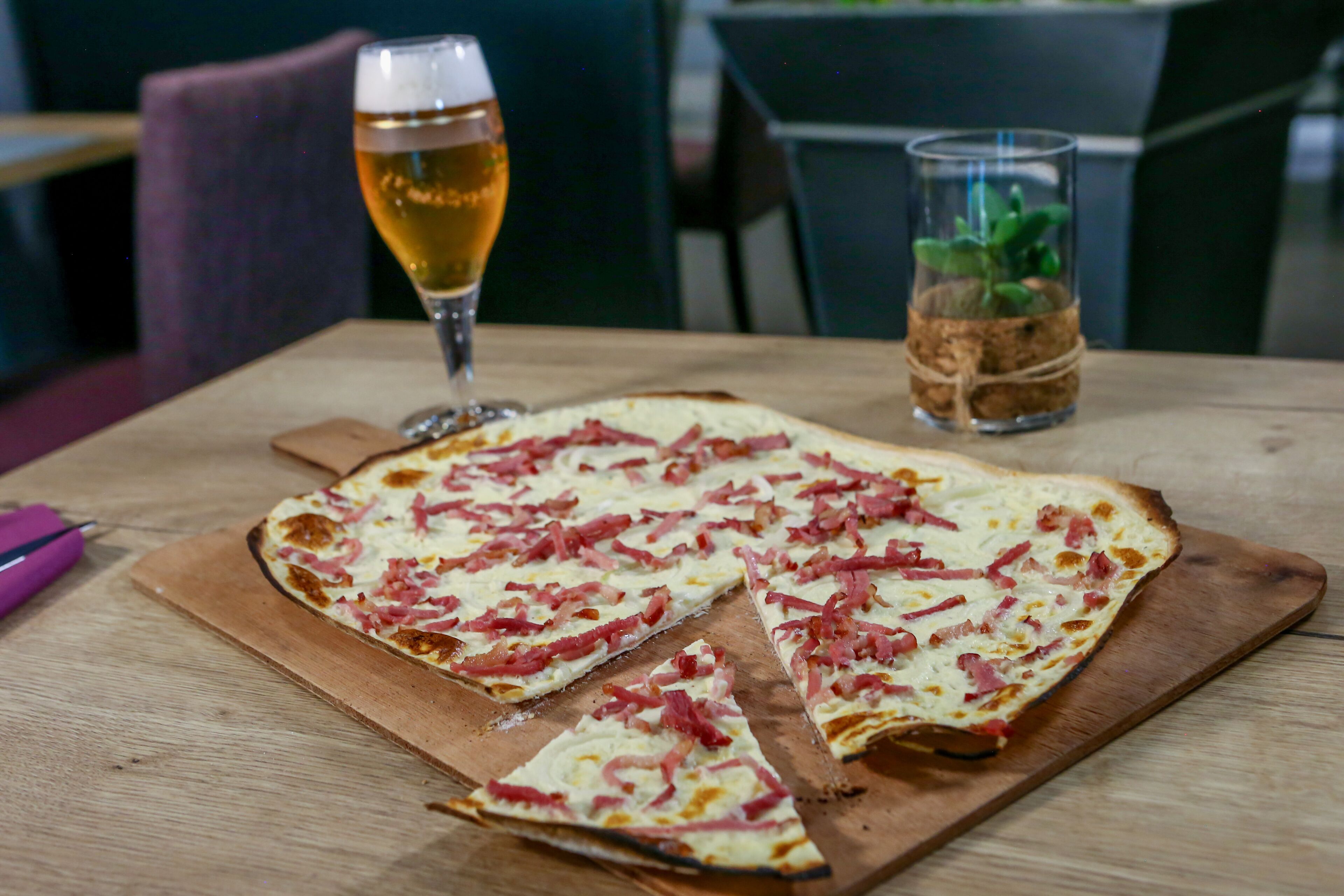 Pizza på træbræt med manglende skiver, et glas øl og et glas med en plante.