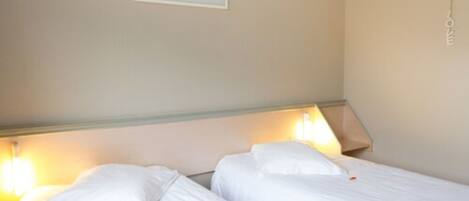 Habitación de hotel con dos camas, cada una con ropa de cama blanca y lámparas a cada lado.