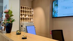 Un mostrador de recepción con detalles de madera, una planta en maceta, un adorno pequeño y un monitor de computadora.