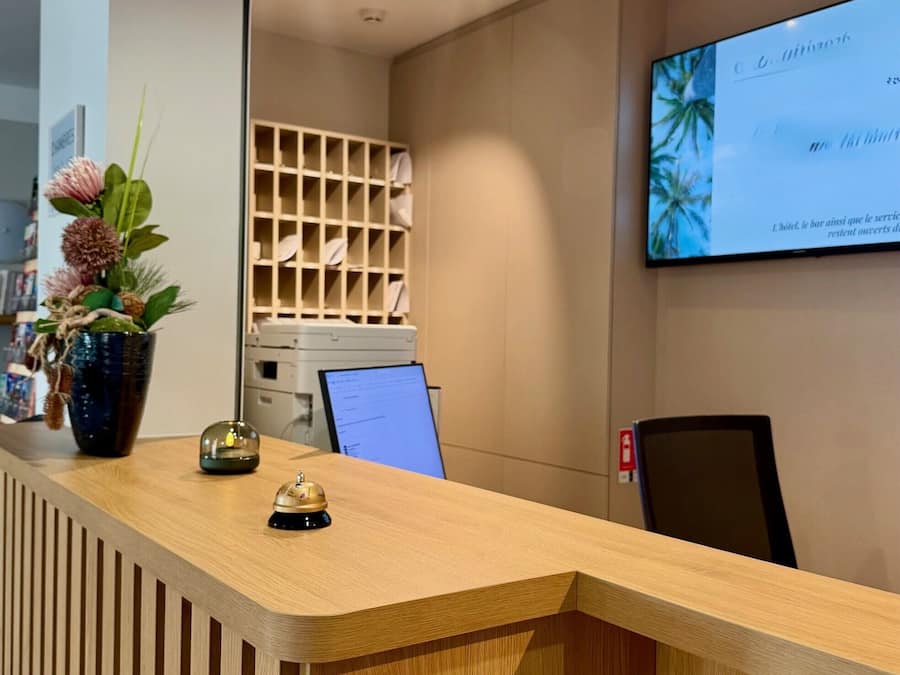 Un mostrador de recepción con detalles de madera, una planta en maceta, un adorno pequeño y un monitor de computadora.