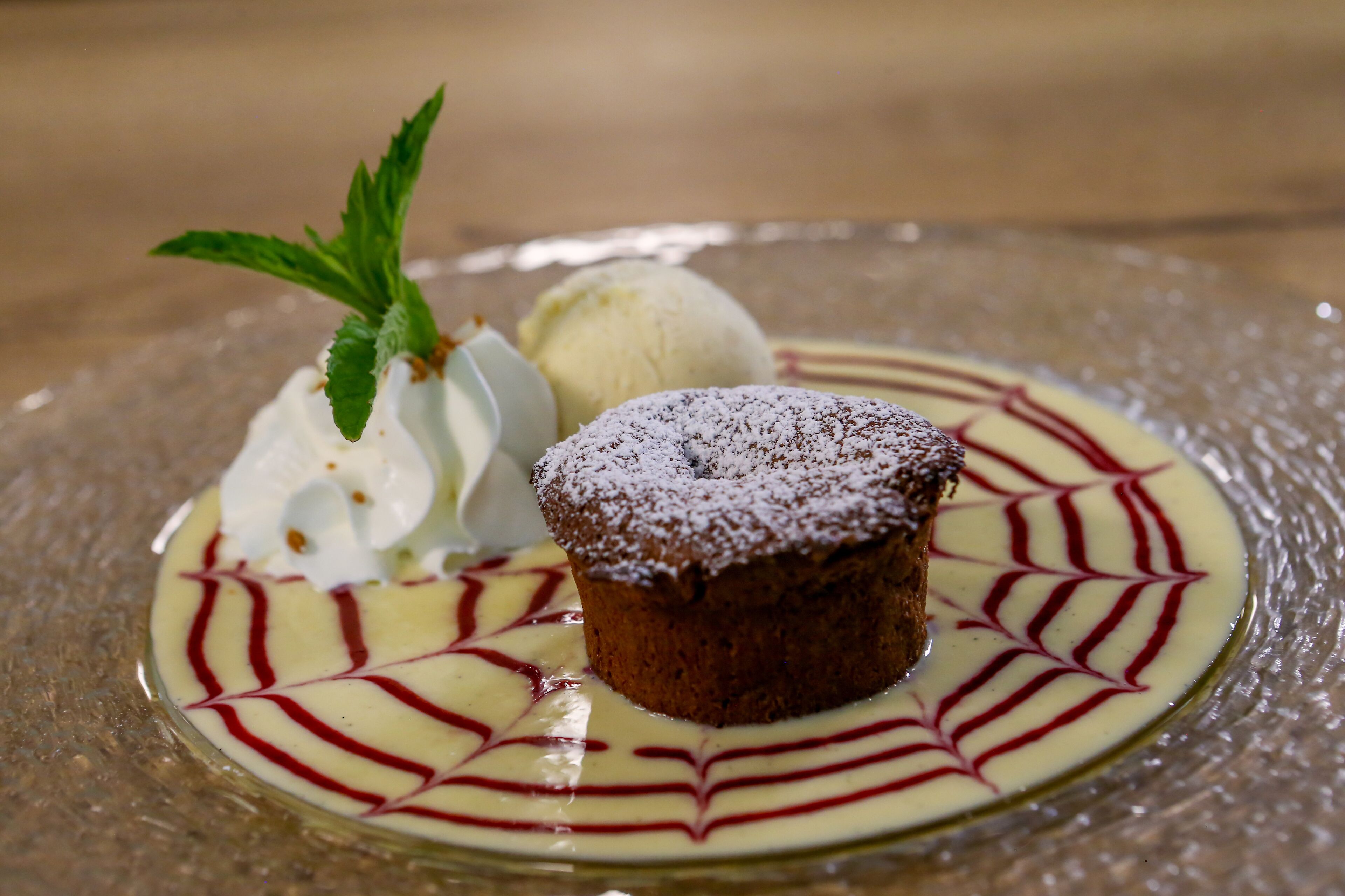 Un postre con una capa de azúcar glas, una bola de helado y una ramita de menta sobre un plato de vidrio.