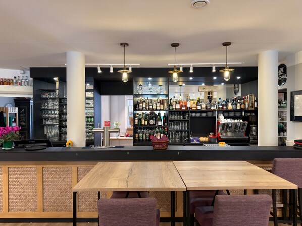 A bar area with a counter, shelves of bottles, glasses, and a coffee machine.