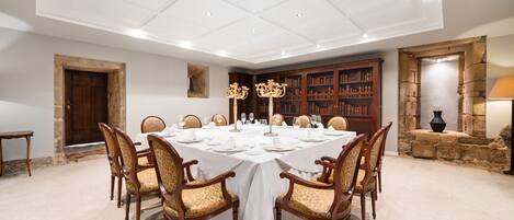 A formal dining room with a large table set for a banquet, surrounded by wooden chairs with patterned upholstery.