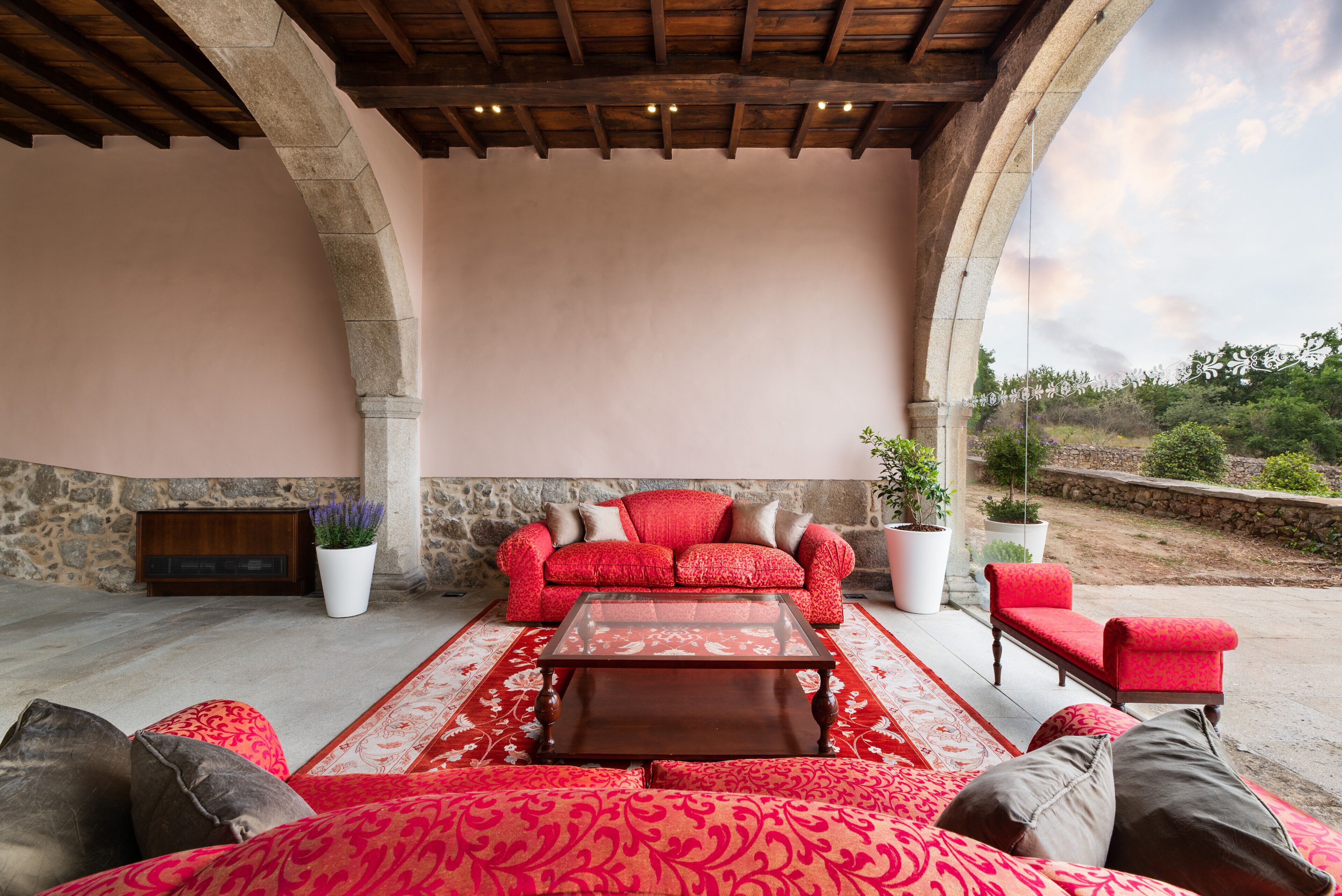 A spacious outdoor seating area with a red sofa set, a coffee table, and potted plants.