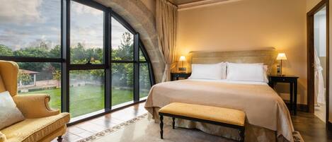 A bedroom with a large window, a bed, a bench, and a chair.