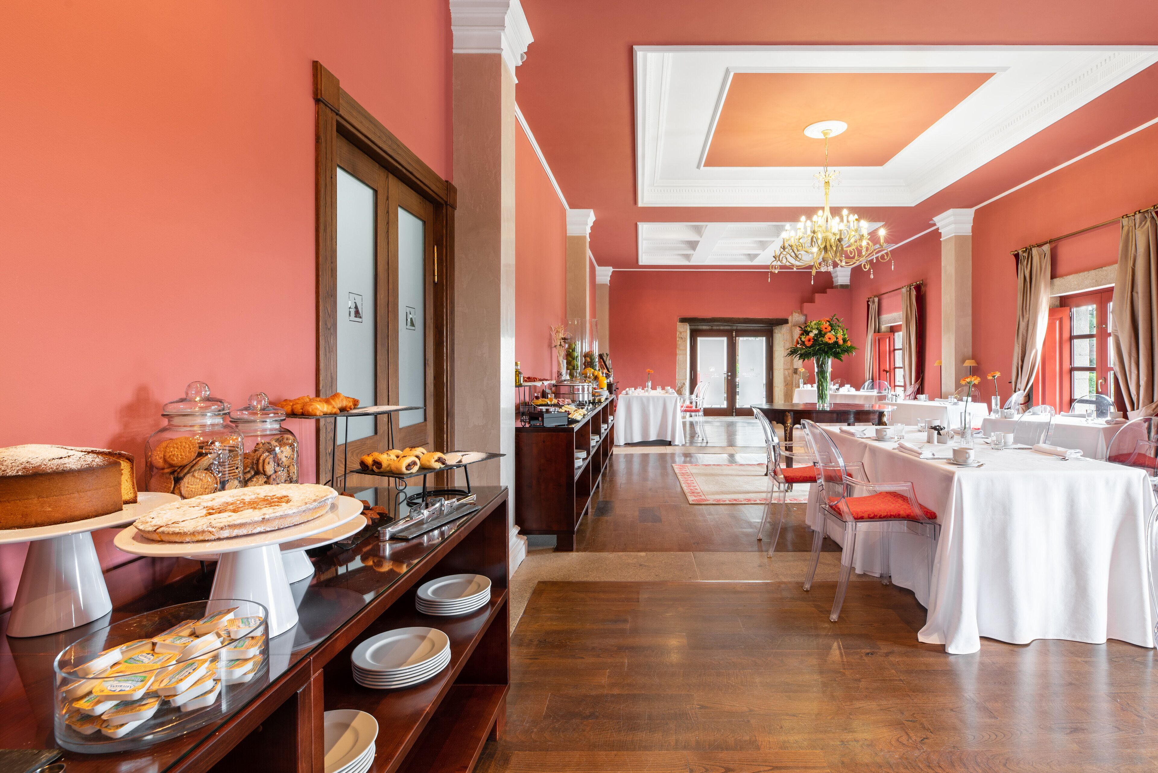 A hotel dining area with a buffet setup, including various food items and a long table with chairs.