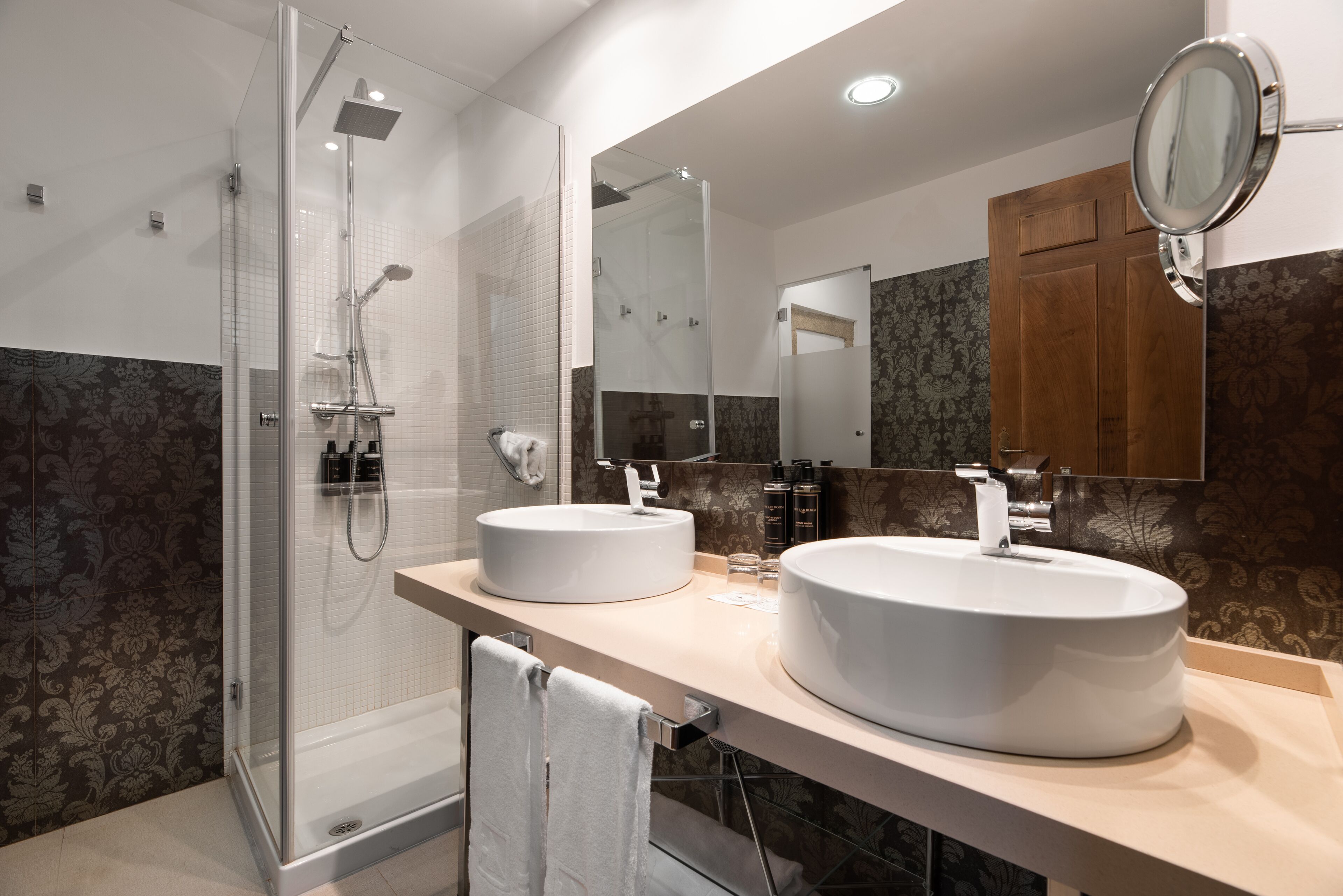 Un baño moderno con ducha de vidrio, dos lavamanos y un espejo grande.
