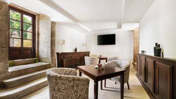 A modern living room with a stone staircase, a flat-screen TV, patterned armchairs, and a wooden coffee table.