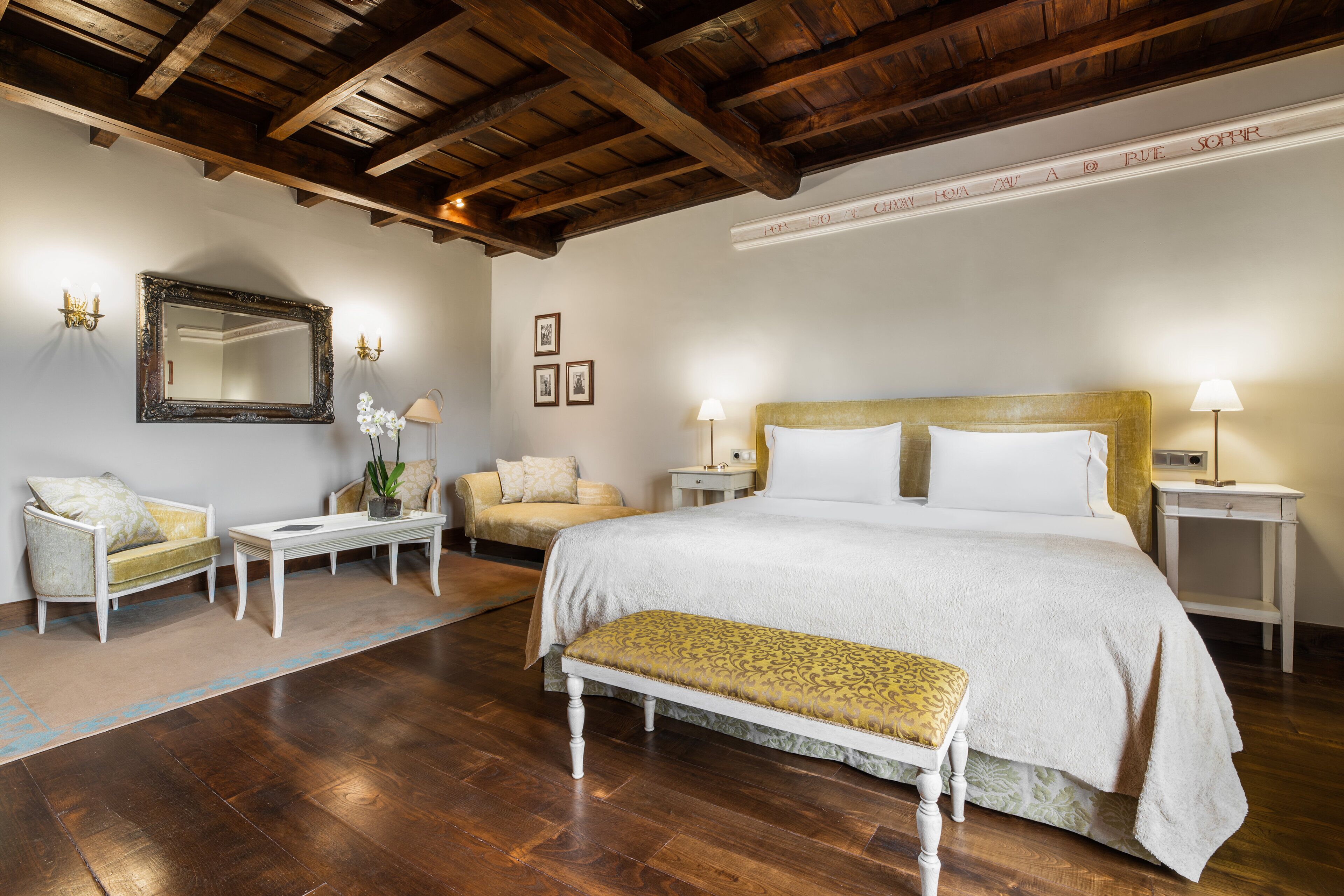 A bedroom with a large bed, bedside tables, a bench, a sofa, and a mirror.