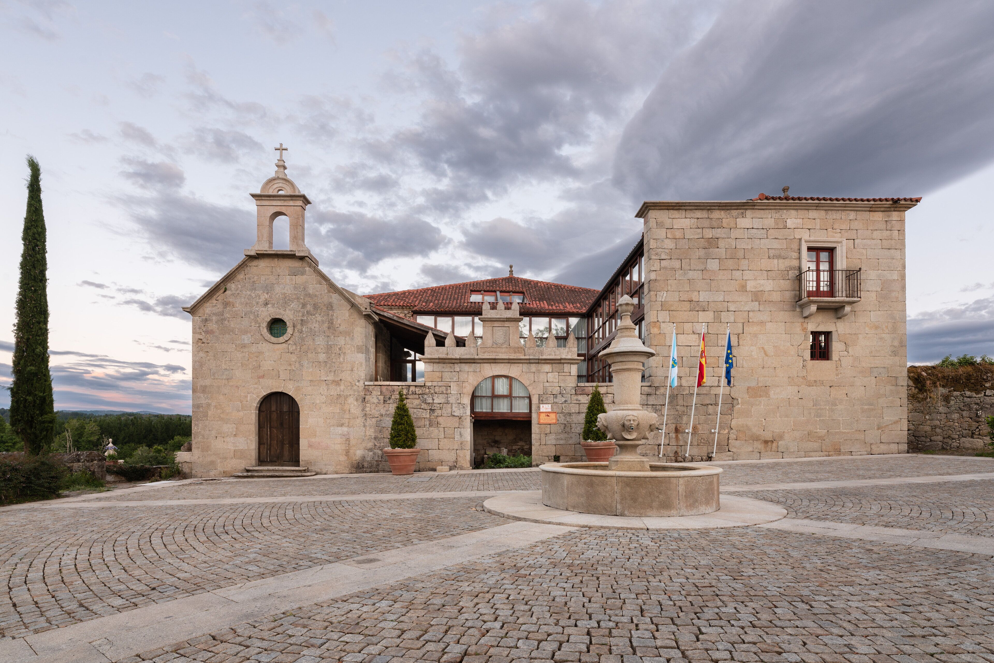 Un edificio histórico con una iglesia, una fuente y banderas.