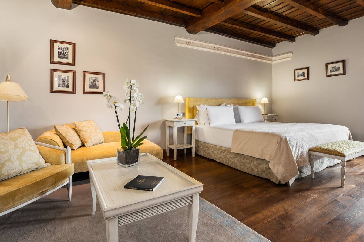 Une chambre d’hôtel avec un lit, un canapé, une petite table avec un livre et une table de chevet avec une lampe.