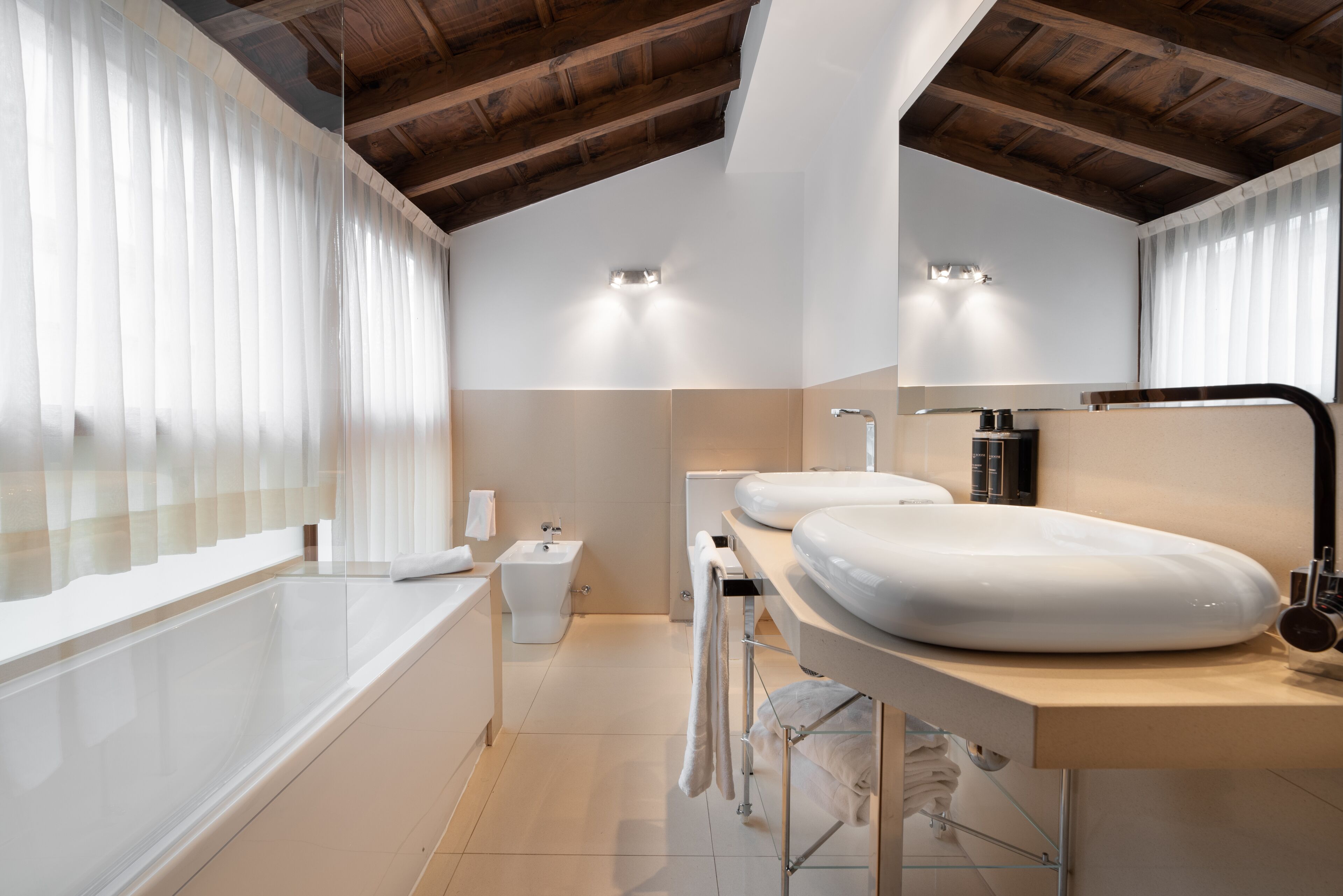 A modern bathroom with a bathtub, two sinks, and a bidet.