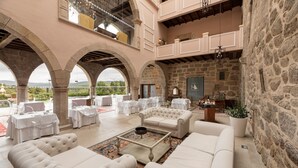 A spacious indoor area with white sofas, a coffee table, and stone walls. Tables and chairs are arranged for dining or socializing.
