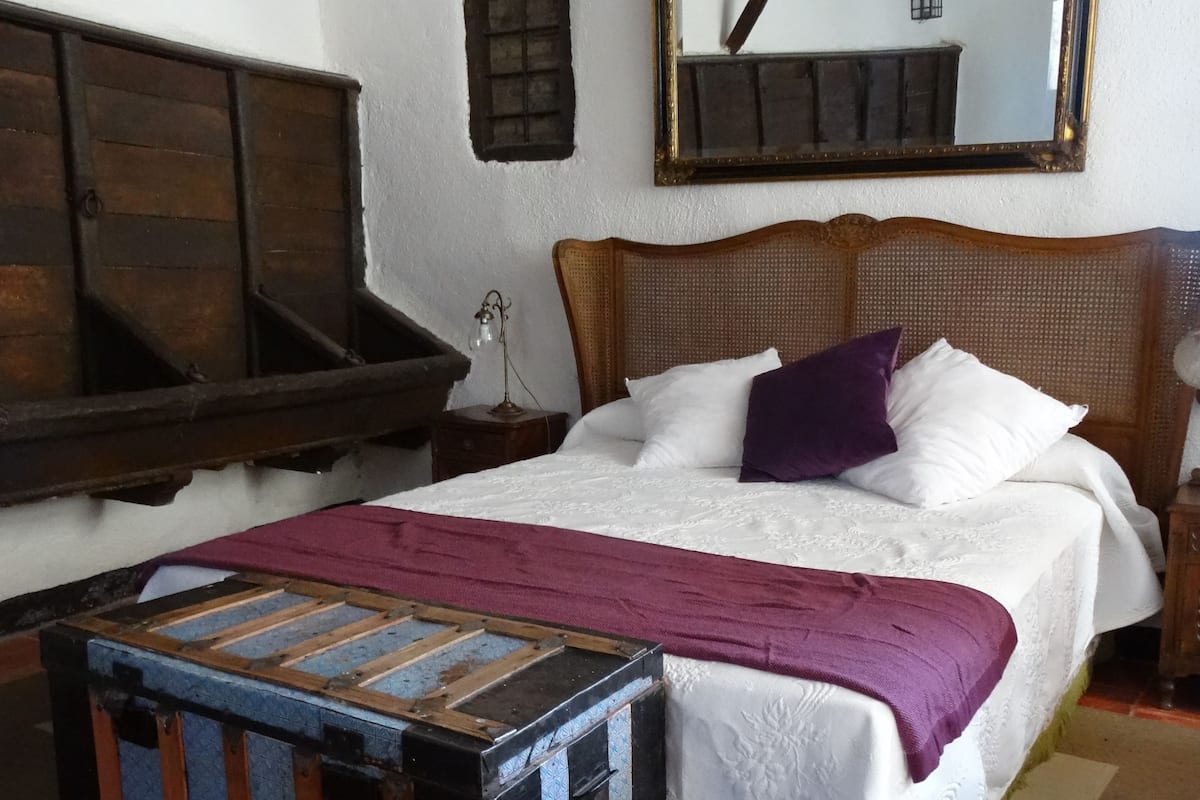 A bedroom with a wooden bed, a headboard, a nightstand, a dresser, and a mirror on the wall.