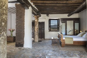 Una habitación rústica con suelo de piedra, cama de madera, un espejo grande y una ventana con rejas.