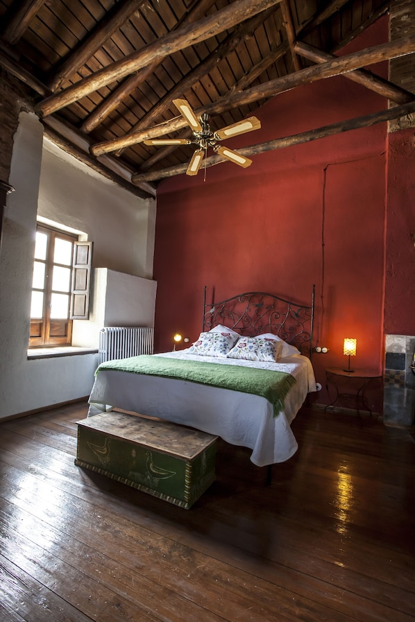 Un dormitorio con techo de madera, una cama con manta verde, una ventana y un radiador.
