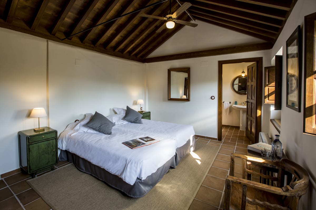A bedroom with a large bed, bedside tables, a wooden ceiling, and a mirror on the wall.