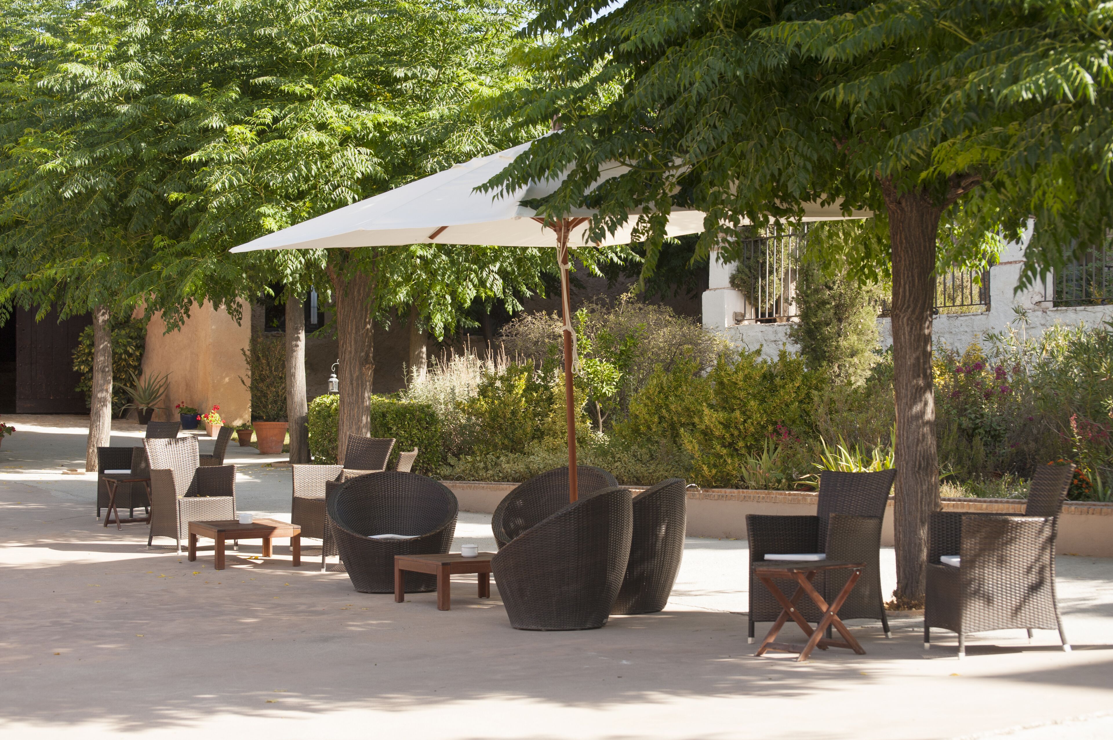 Un patio al aire libre con mobiliario de mimbre, una mesa y un paraguas grande que da sombra.
