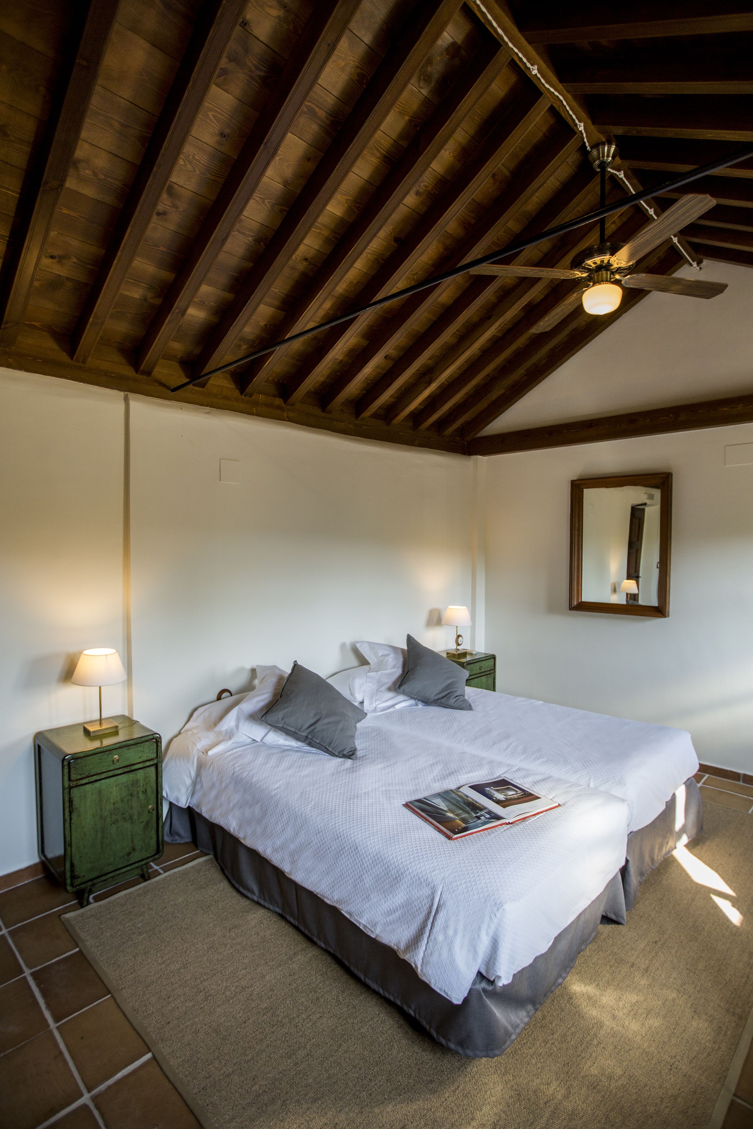 A bedroom with a large bed, two bedside tables with lamps, a ceiling fan, and a mirror on the wall.