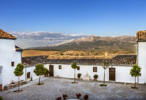 Un patio con edificios blancos, plantas en macetas y montañas al fondo.