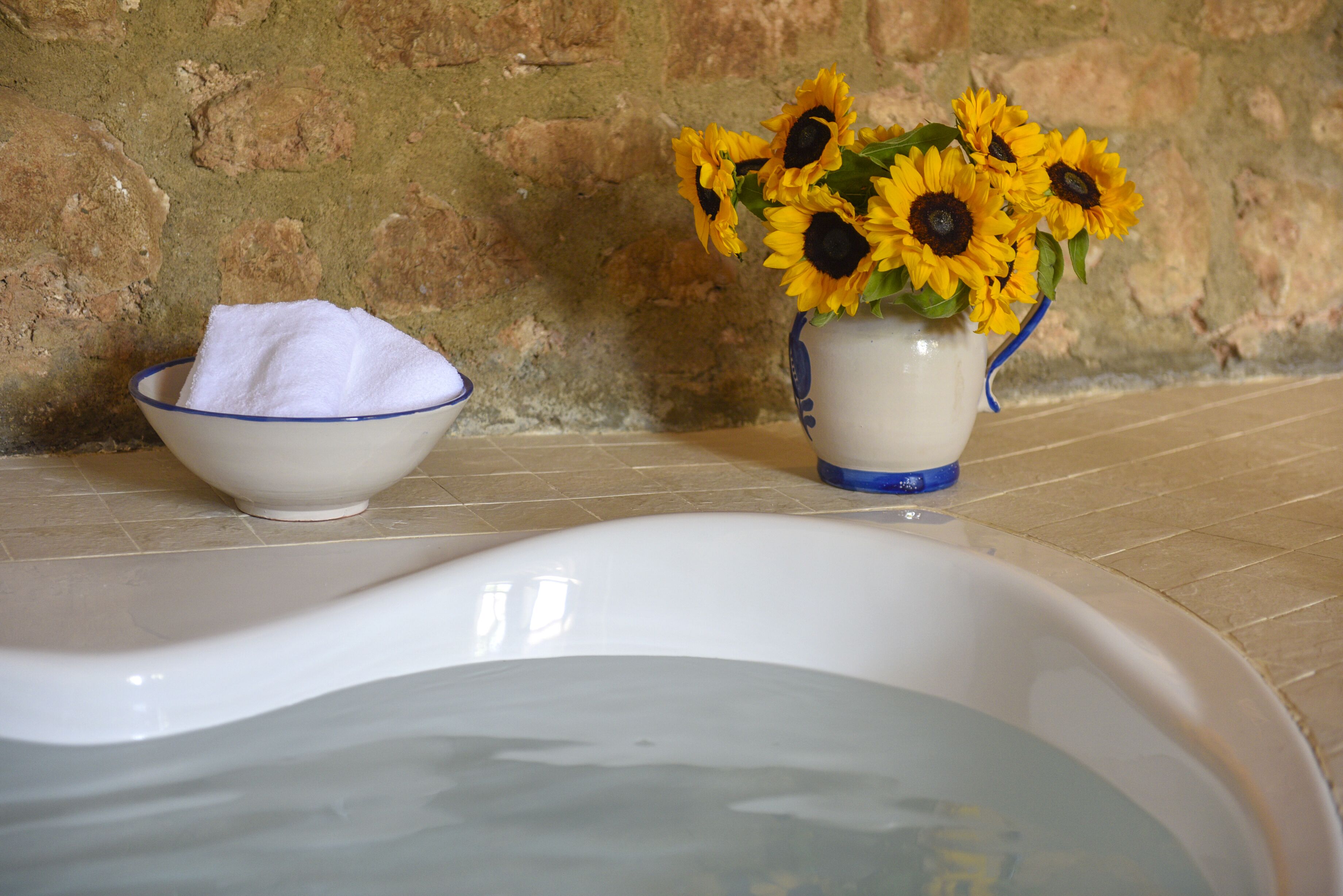 Une baignoire à l’intérieur blanc, un bol avec une serviette blanche et un vase avec des tournesols.
